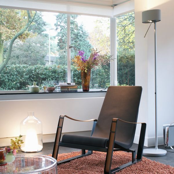 Heller Wohnraum mit großem Fenster, Lesesessel und der Stehleuchte Diogenes von Belux am rechten Bildrand