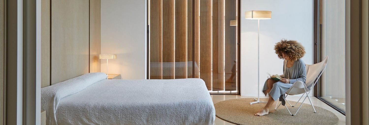 Weiße Bogenlampe Kyudo mit dünnem Lichtband über einem braunen Ledersofa vor einer Betonwand